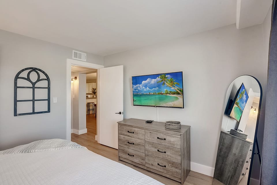 Unwind in your spacious bedroom featuring a large TV with tropical views, ample dresser storage, and elegant mirror for getting ready.