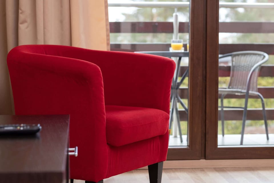 A red armchair placed near a large window with a view of the balcony and outdoors.
