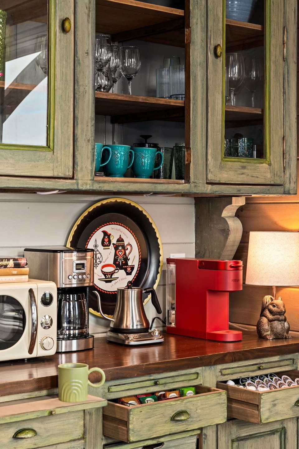 A well-appointed coffee bar featuring a drip coffee maker, tea kettle, Keurig, pour-over carafe, grinder, French press, percolator, and milk-frother—stocked with Keurig pods, creamers, and an assortment of teas.