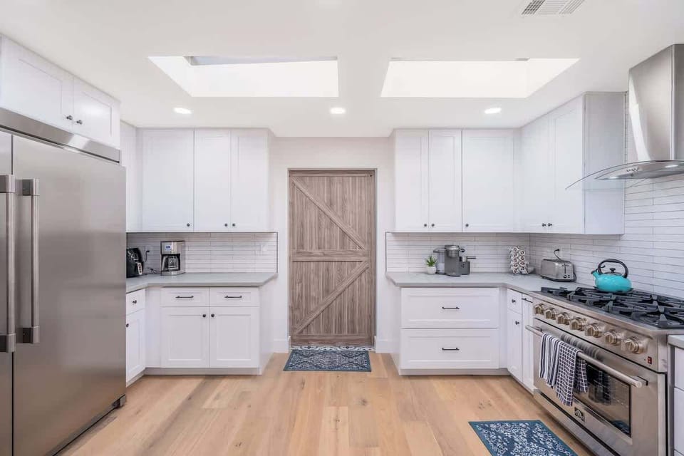 Step into your bright, spacious kitchen with gleaming white cabinets, stainless steel appliances, and natural light pouring through skylights above, ready for your next meal.