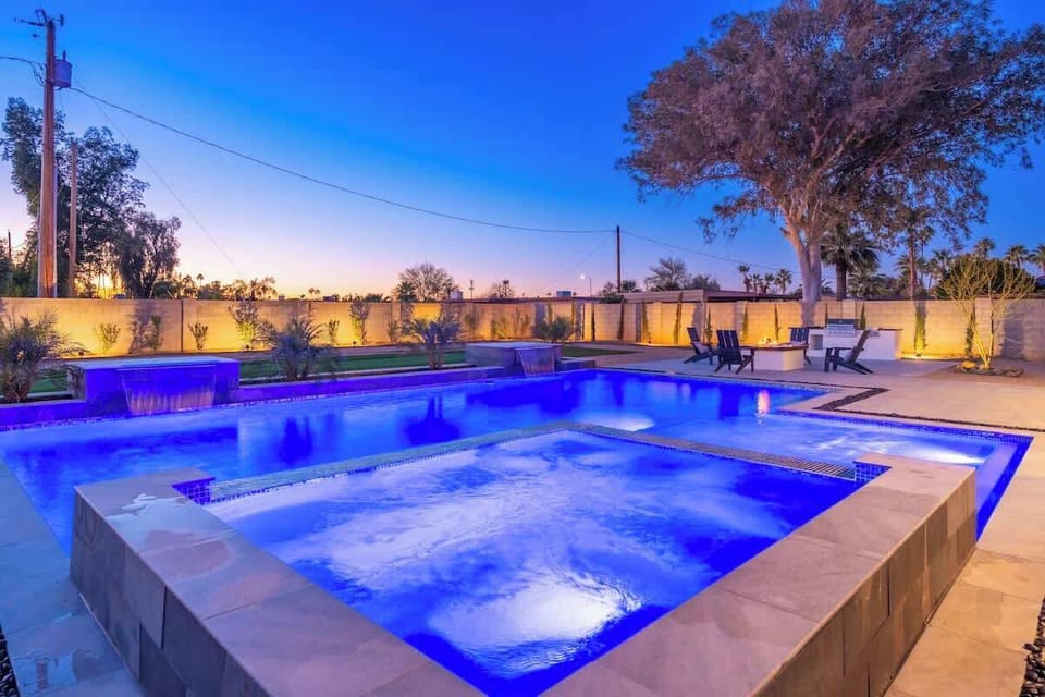 A stunning resort-style pool and spa glowing at twilight, surrounded by lush landscaping and modern outdoor seating areas perfect for evening relaxation.