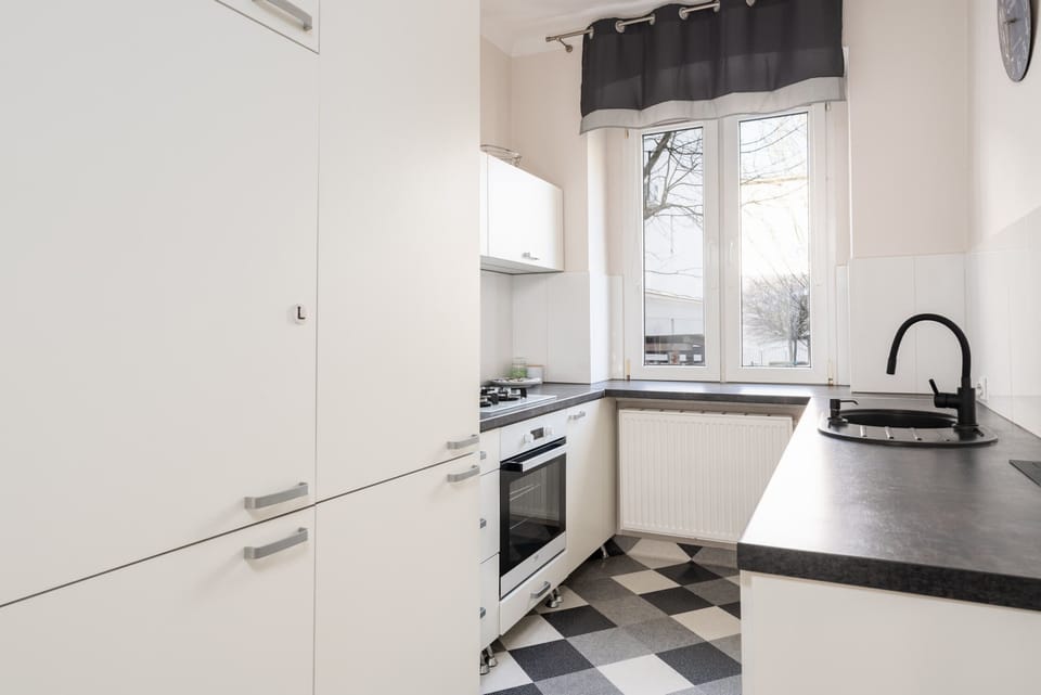 A compact kitchen featuring a bright window, white cabinetry, and a clean design with a black countertop.