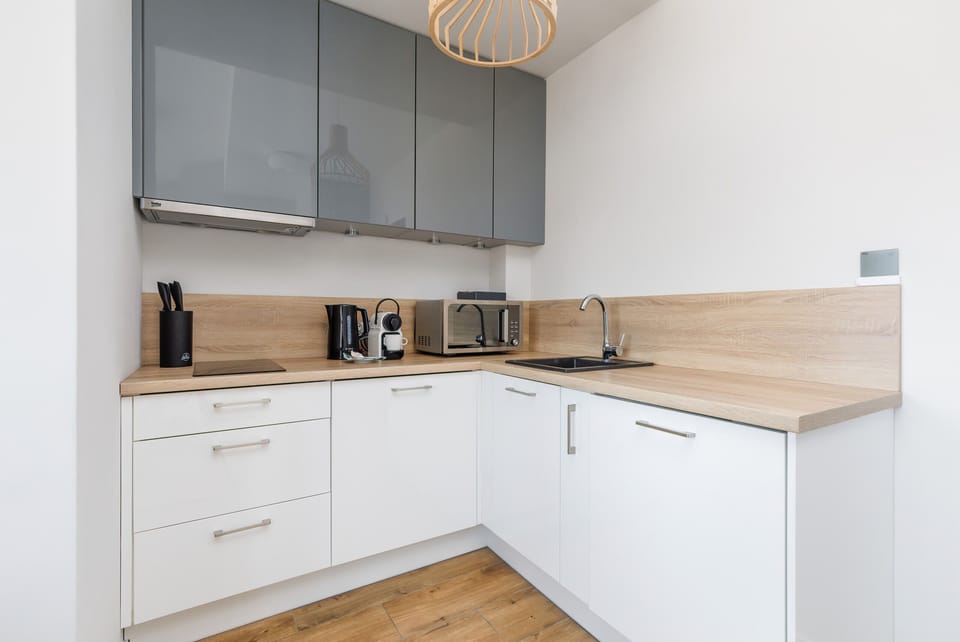 A sleek kitchen with white cabinetry, light wooden countertops, and a neat arrangement of appliances and shelves.