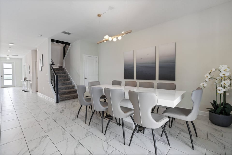 Enjoy a spacious dining area featuring a sleek white table and modern gray chairs, all set on elegant marble flooring. Natural light fills the space, creating a warm, inviting atmosphere with minimalist decor.