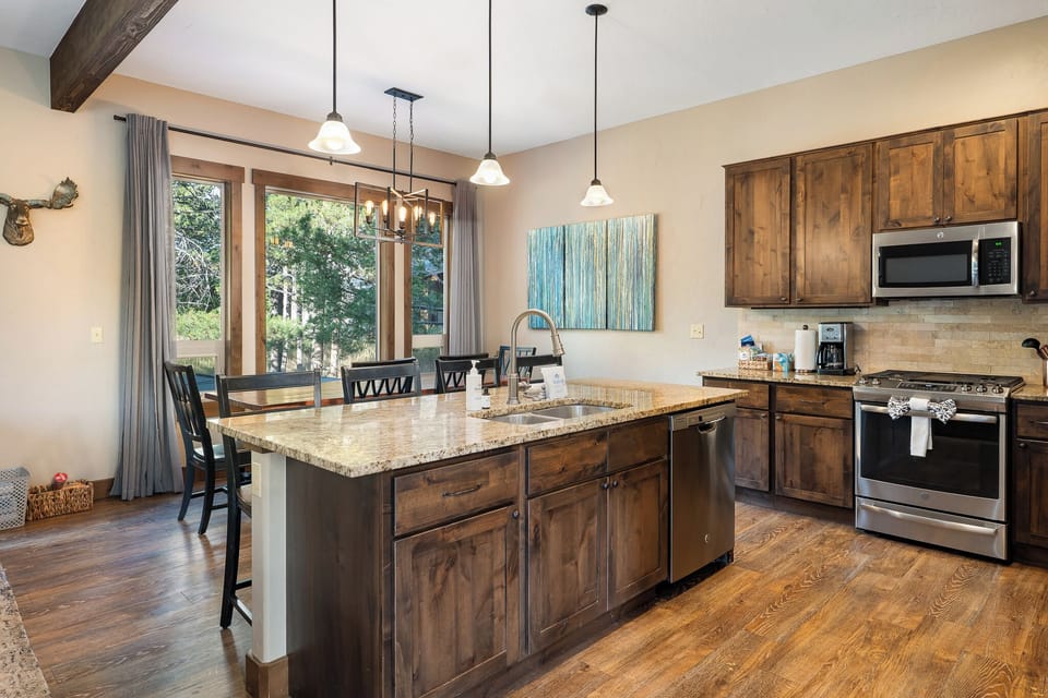 - Kitchen island with sink and granite countertops for prep   - Pendant lighting highlights warm wood cabinetry and floors   - Open layout flows into dining and living areas with ease