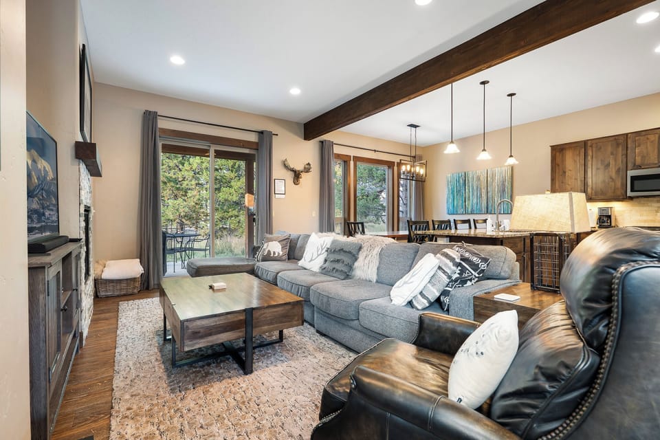 - Spacious living room with sectional sofa and rustic decor   - Large windows bring in natural light and scenic forest views   - Open concept connects seamlessly to kitchen and dining