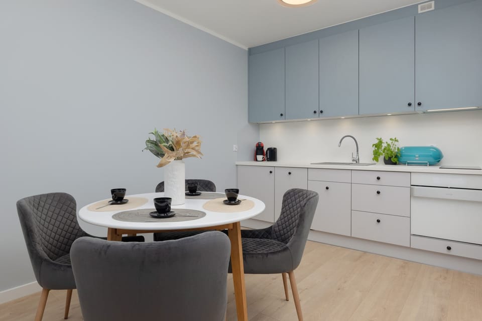 A compact dining space with a round table and gray chairs, next to a sleek kitchenette.