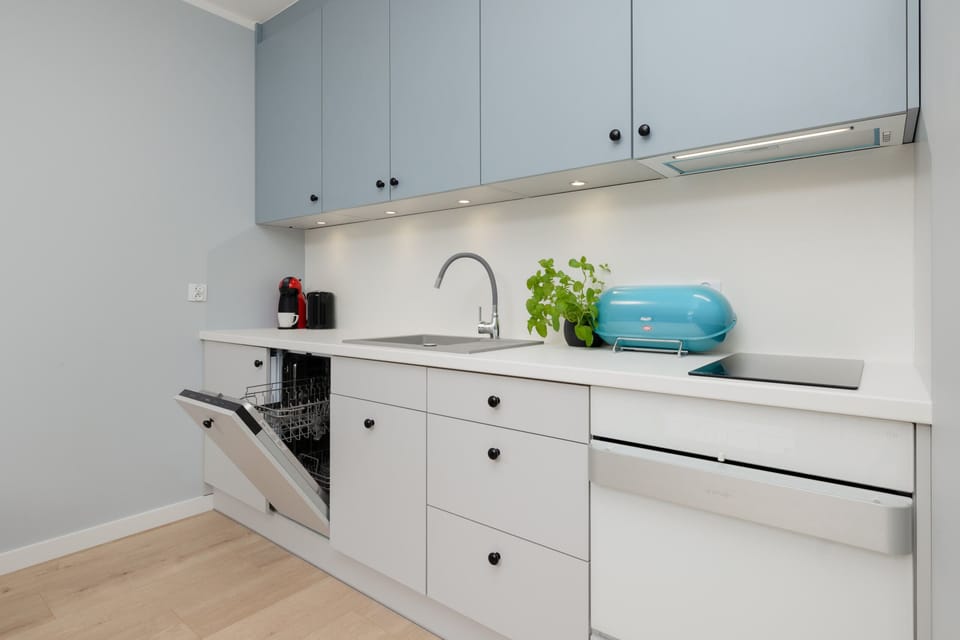 A minimalist kitchenette with white cabinetry, open shelving, and a pop of color from kitchen accessories.