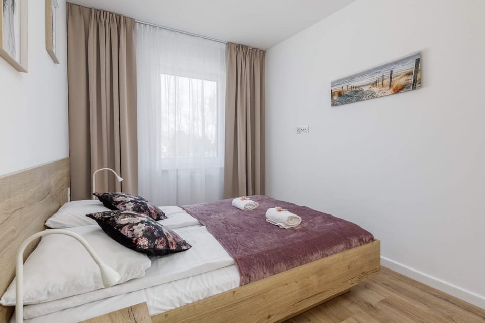 A bedroom with a wooden bed frame, gray bedding, and floor-to-ceiling curtains.