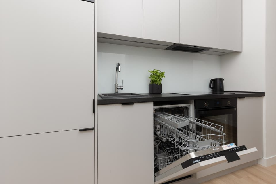 A sleek and compact kitchen with white cabinetry, black countertops, and modern appliances.