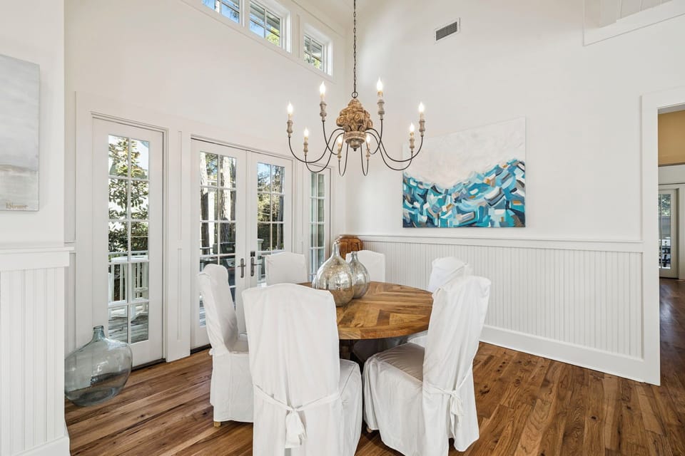 Gather around your elegant dining table under soft chandelier light, with French doors opening to outdoor views.