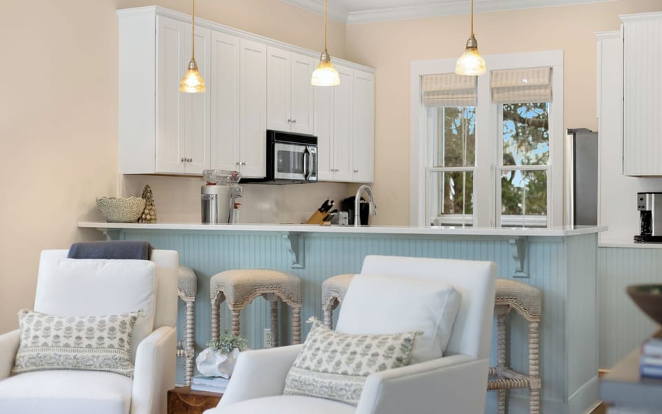 Relax in your bright coastal kitchen featuring white cabinetry, modern appliances, and charming pendant lighting perfect for morning coffee.