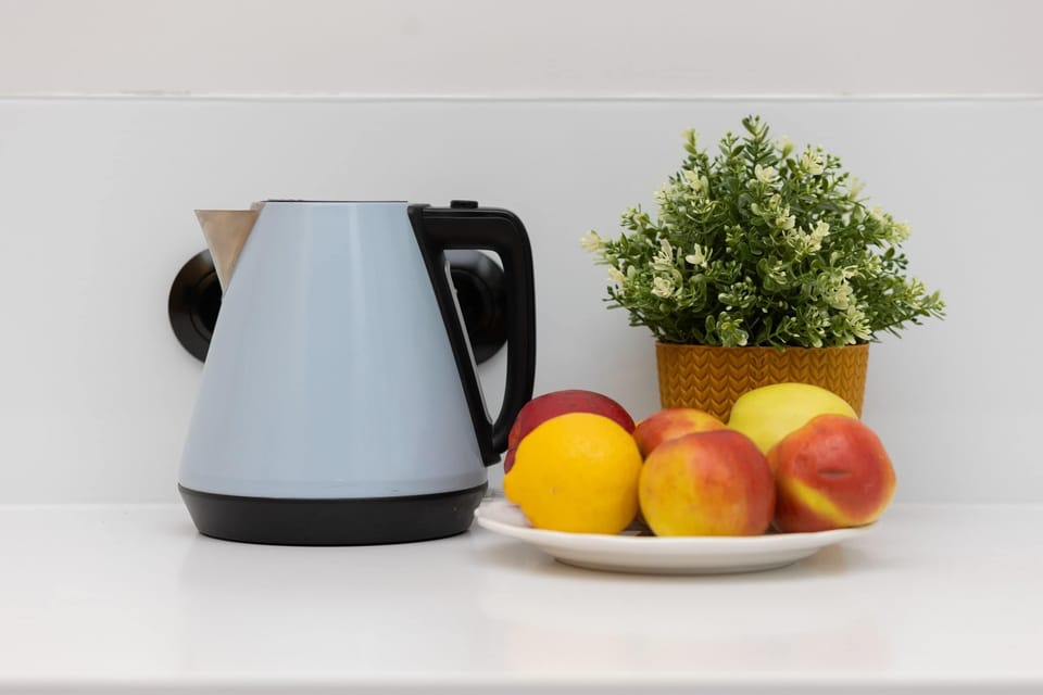 Kitchen counter decorated with a kettle, fresh fruits, and a small plant, creating a welcoming and homely vibe.
