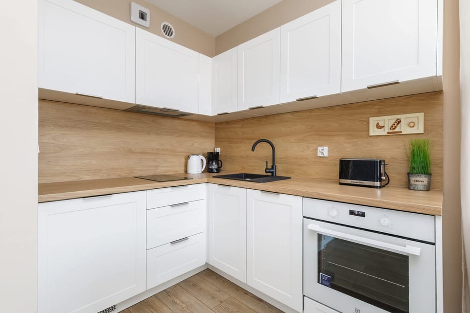 A well-organized kitchen with white cabinetry, a wooden countertop, and modern appliances. The backsplash is kept simple, enhancing the clean aesthetic.