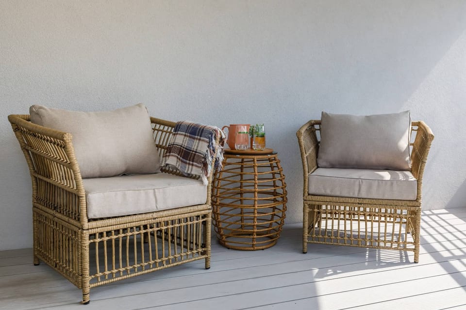 A cozy wicker chair with a plaid throw blanket, placed in a sunlit corner of the balcony. This setup offers a perfect spot for relaxation.