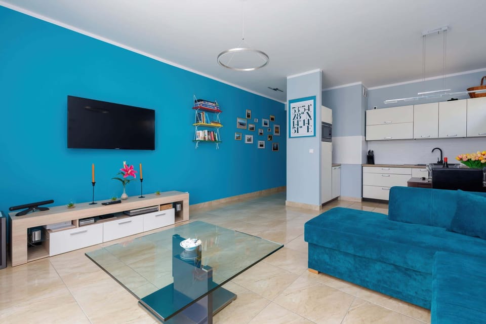 A bright, modern living room with a turquoise sofa, decorative pillows, and a flat-screen TV mounted on the wall.