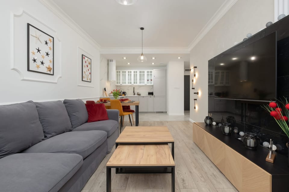 A view of the living room with a large flat-screen TV, a grey sofa, and a coffee table, ideal for leisure and entertainment.


