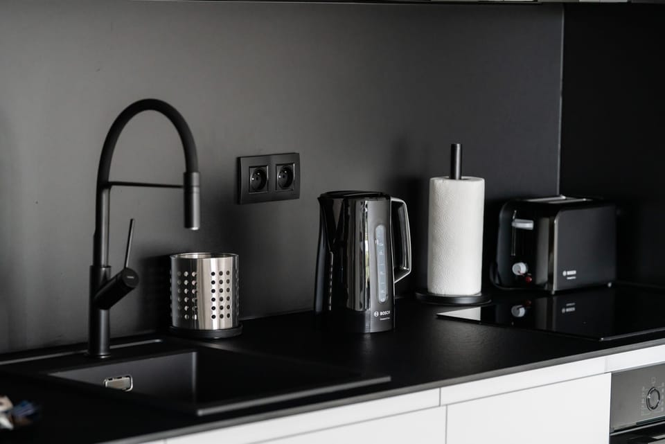 A sleek and functional kitchen counter with a black sink, electric kettle, coffee maker, and toaster.
