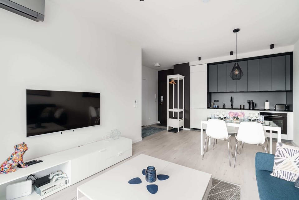 A spacious living room with a flat-screen TV, white furniture, and an adjoining dining area.
