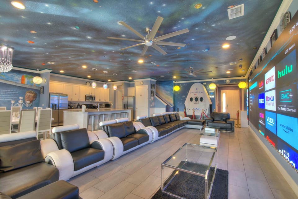 Experience a cosmic adventure in this space-themed living room with a massive TV, plush seating, and a fully equipped kitchen.