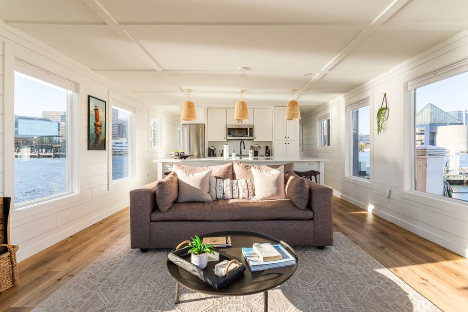 Open-concept living area with designer sleeper sofa, coffered ceilings, and 360° waterfront views of the Inner Harbor and National Aquarium.