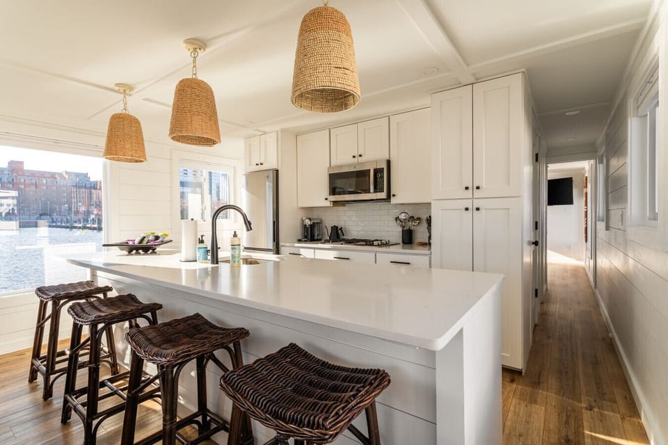 Fully stocked galley kitchen with a quartz island, four-seat breakfast bar, woven pendant lights, and harbor views through every window.