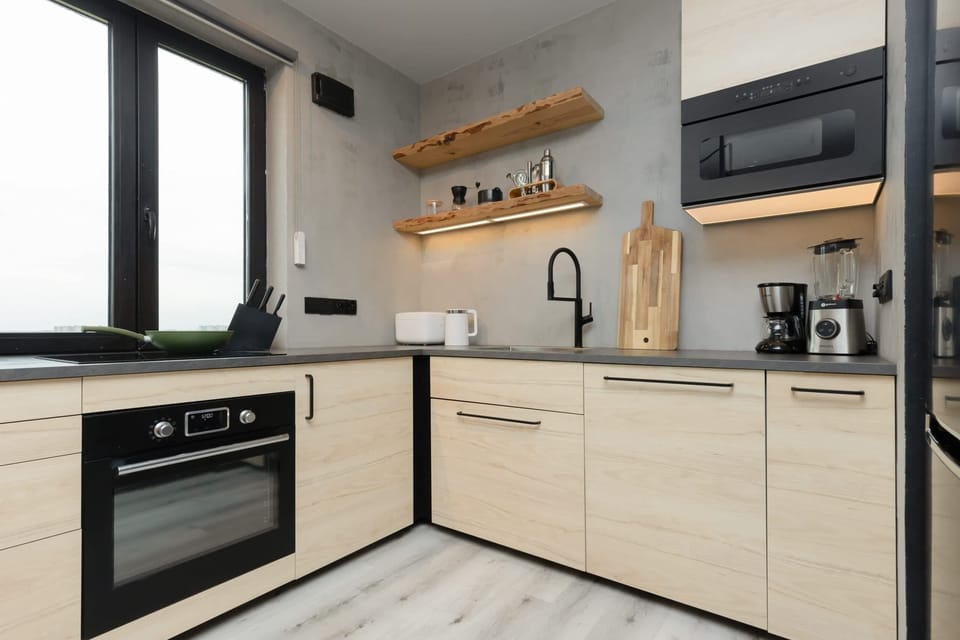A contemporary kitchen with light wood cabinetry, black accents, and high-end appliances.