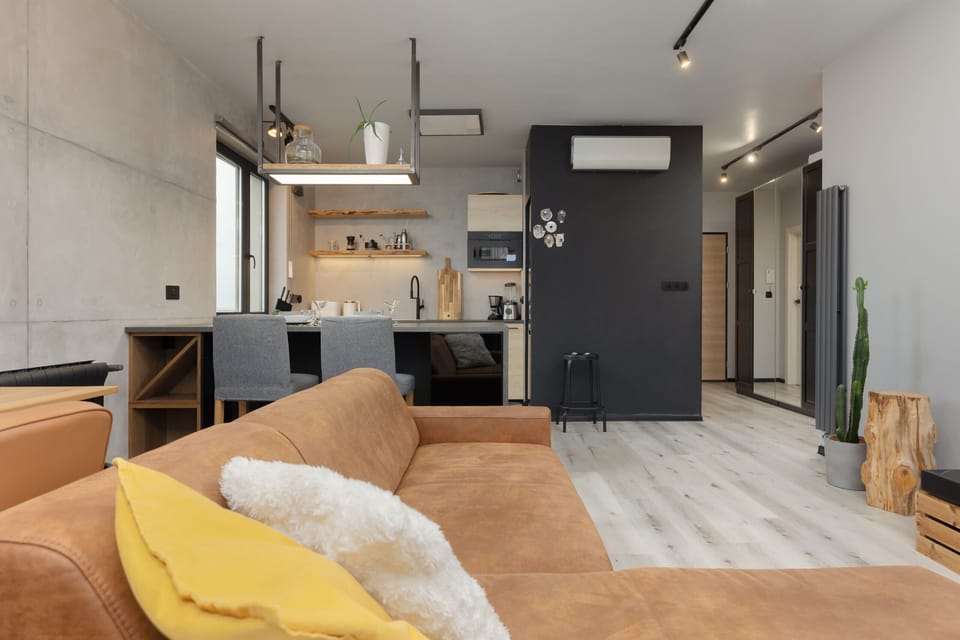 A modern, industrial-style living room with concrete walls, a comfortable orange sofa, and sleek lighting.