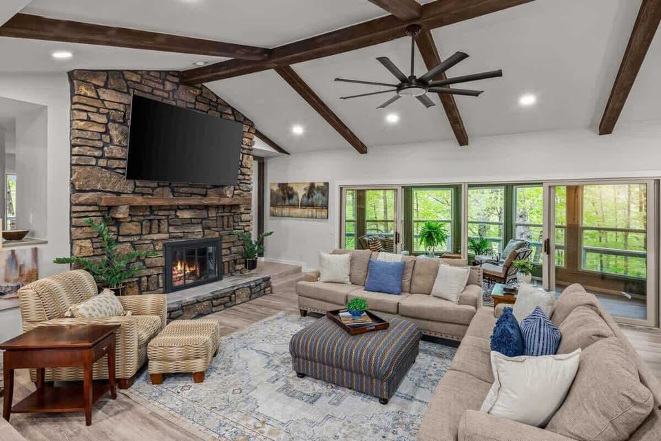 Unwind by the stone fireplace in this light‑filled living room with vaulted ceilings, exposed beams and a 75″ smart TV.