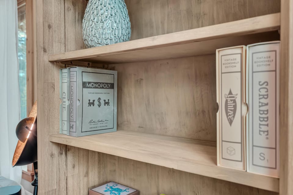 Wood bookshelf in bedroom holds vintage edition board games, with natural light from nearby window.