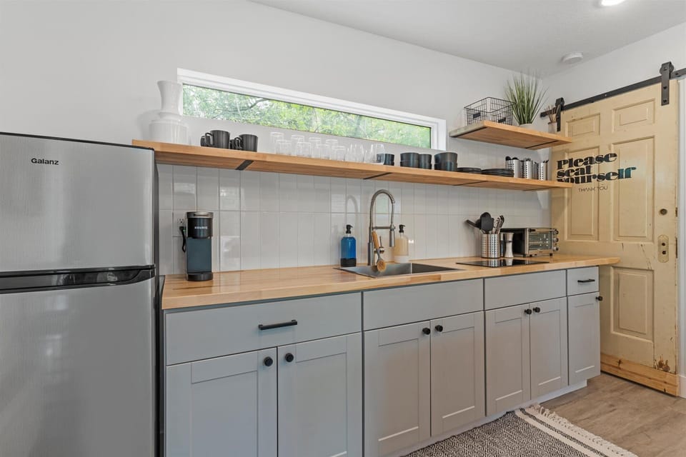 Kitchenette with refrigerator, electric cooktop, toaster oven, Keurig K-Cup coffee maker, and wooded views.