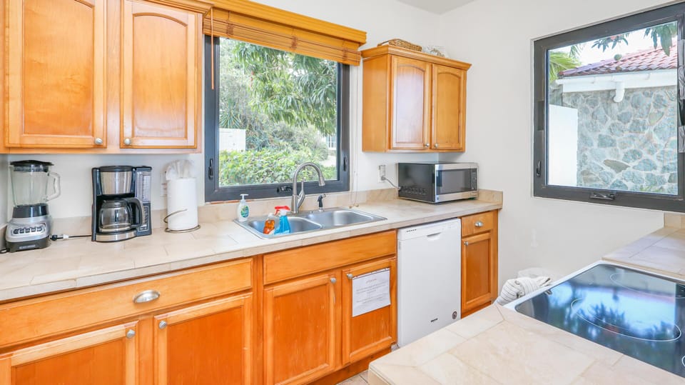 Natural light fills the kitchen with honey-toned wood cabinets, tiled countertops, and stainless steel appliances.