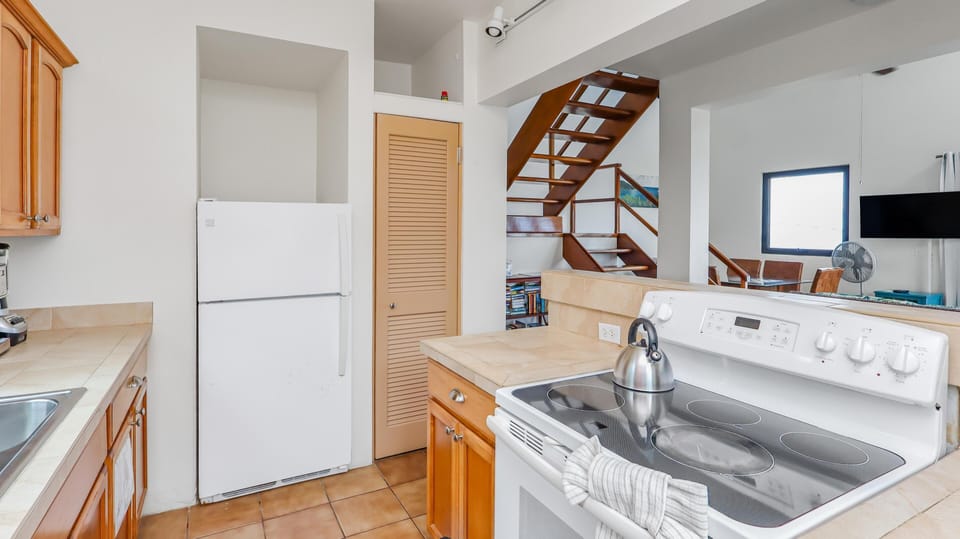 Tile countertops and honey-toned cabinetry surround the white electric stove and refrigerator in the kitchen.