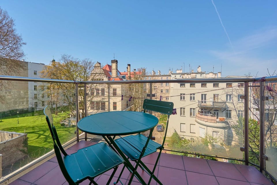A charming balcony with green chairs, a table, and a view of historic buildings.