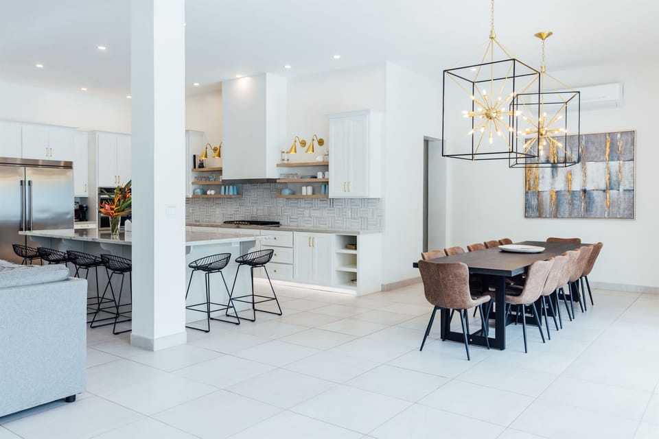 Spacious kitchen offering ample seating options at a  modern table and counter bar, illuminated by large, beautiful light fixtures.