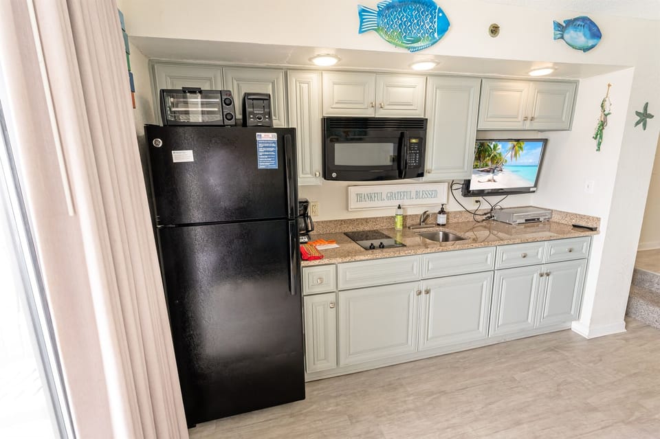 - This fully equipped kitchen blends functionality with coastal charm - Enjoy the convenience of a refrigerator, microwave, and cooktop, all set against a stylish backdrop - Whether it’s morning coffee or a beach picnic prep, this space has you covered