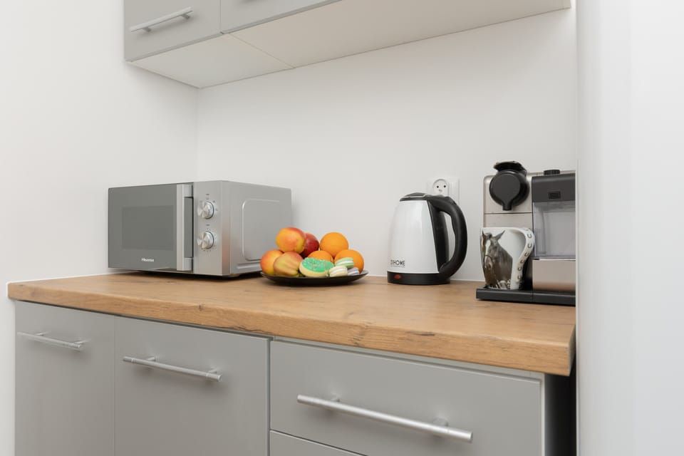 A compact kitchen area with a microwave, cabinets, and a clean, modern design, featuring light tones.