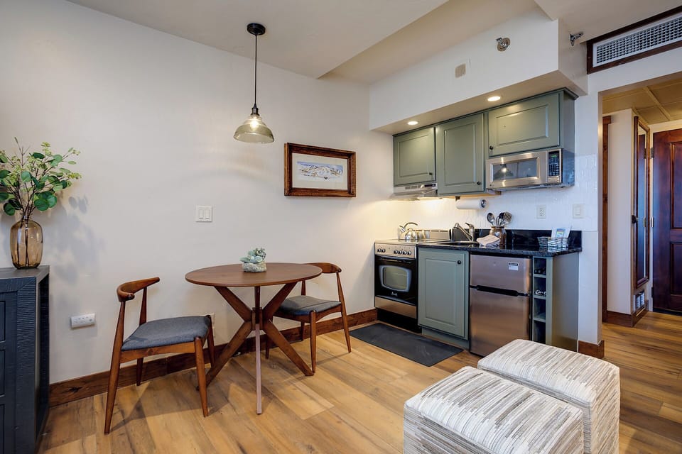 Your stylish kitchenette and dining nook blend seamlessly, offering everything you need to whip up meals in sage-green cabinetry while savoring them at your intimate wood table.