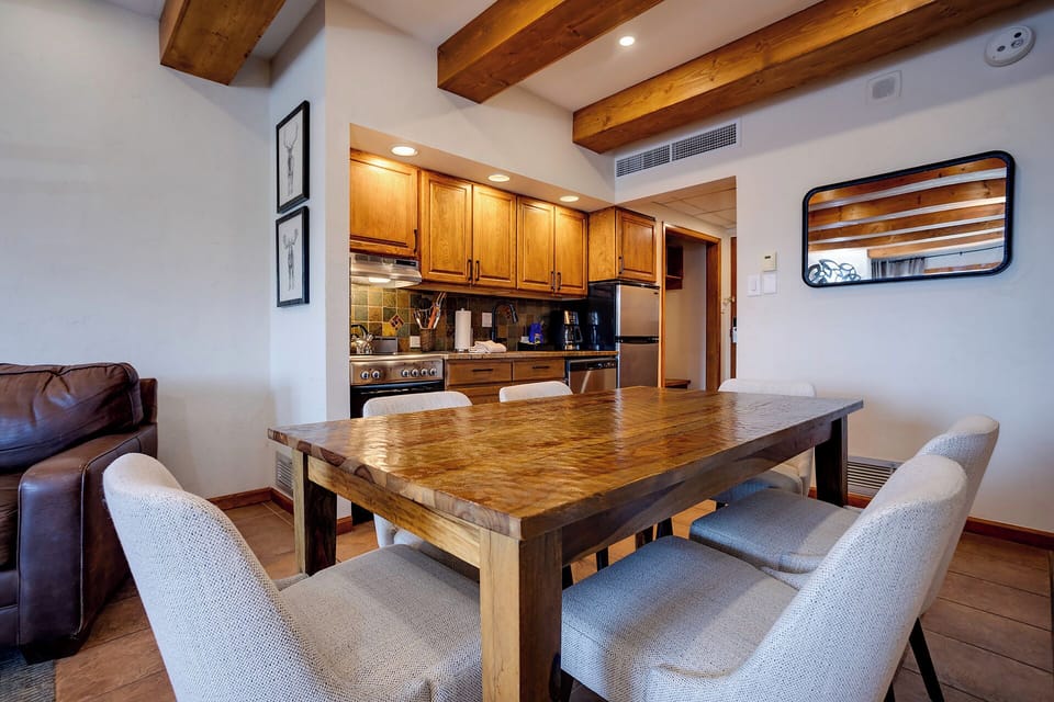Step into your mountain retreat where rustic wood beams crown a fully equipped kitchen, perfect for preparing memorable meals around the handcrafted dining table.