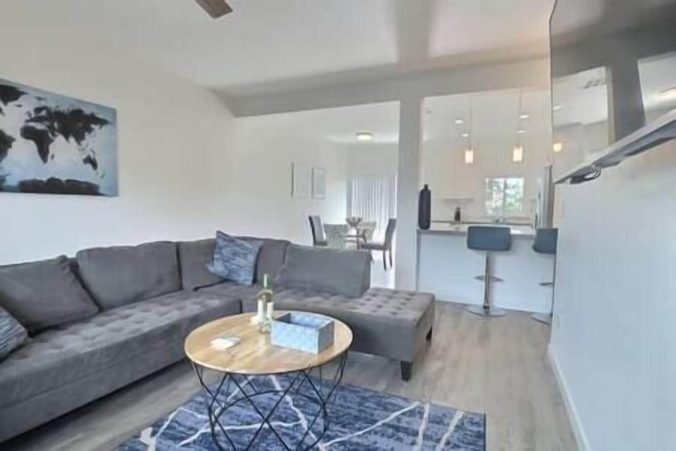 Spacious living room with L-shaped couch, smart TV, open kitchen, dining nook, and patio views (2)