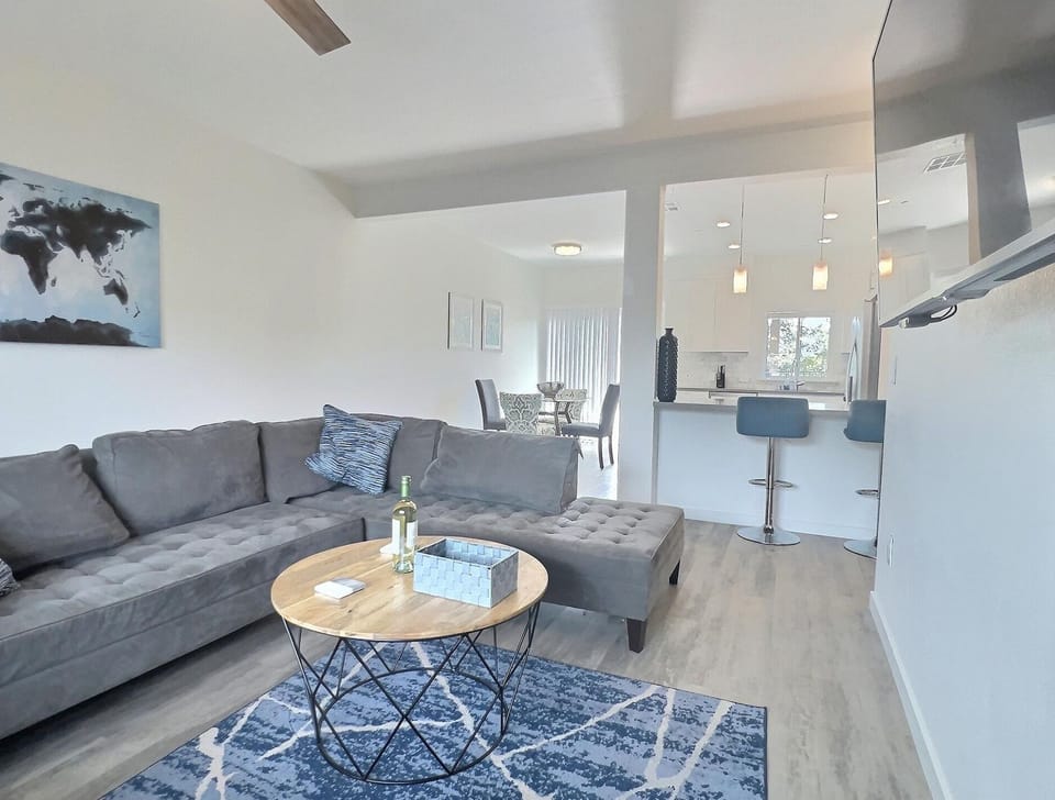 Spacious living room with L-shaped couch, smart TV, open kitchen, dining nook, and patio views (1)