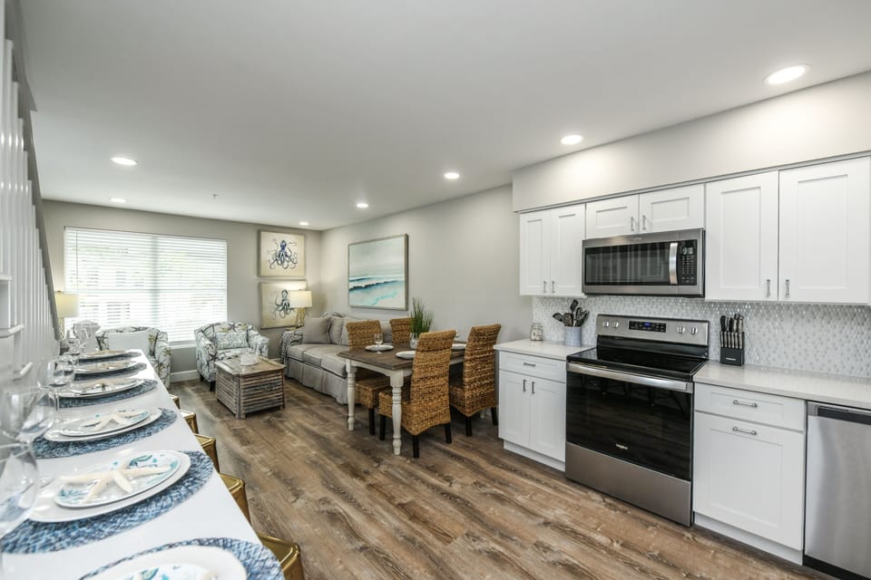 Crisp white cabinetry and stainless steel appliances anchor this fully equipped kitchen, open to the dining and living spaces.