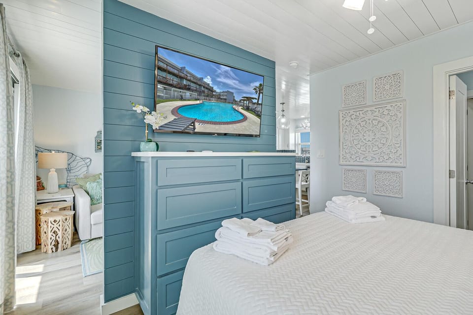 Unwind in your coastal bedroom featuring fresh linens, calming blue tones, and a large TV for your evening entertainment.