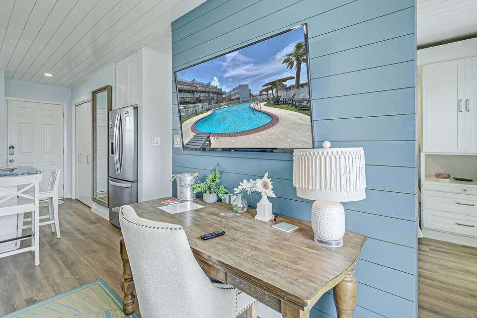 Relax at your coastal dining table while watching poolside views on the large TV, blending indoor comfort with outdoor charm.
