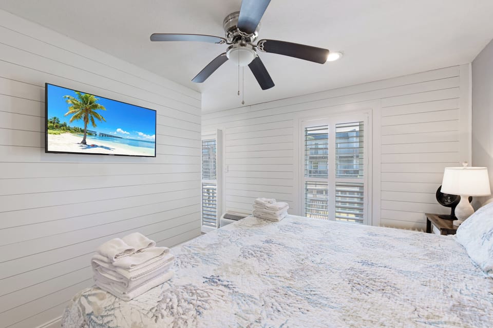 Your peaceful bedroom features coastal charm with shiplap walls, ceiling fan, and tropical TV views for ultimate relaxation.