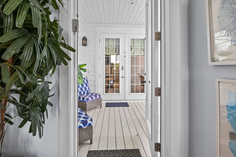 Step onto your private covered porch where vibrant blue-patterned seating awaits beneath crisp white beams.