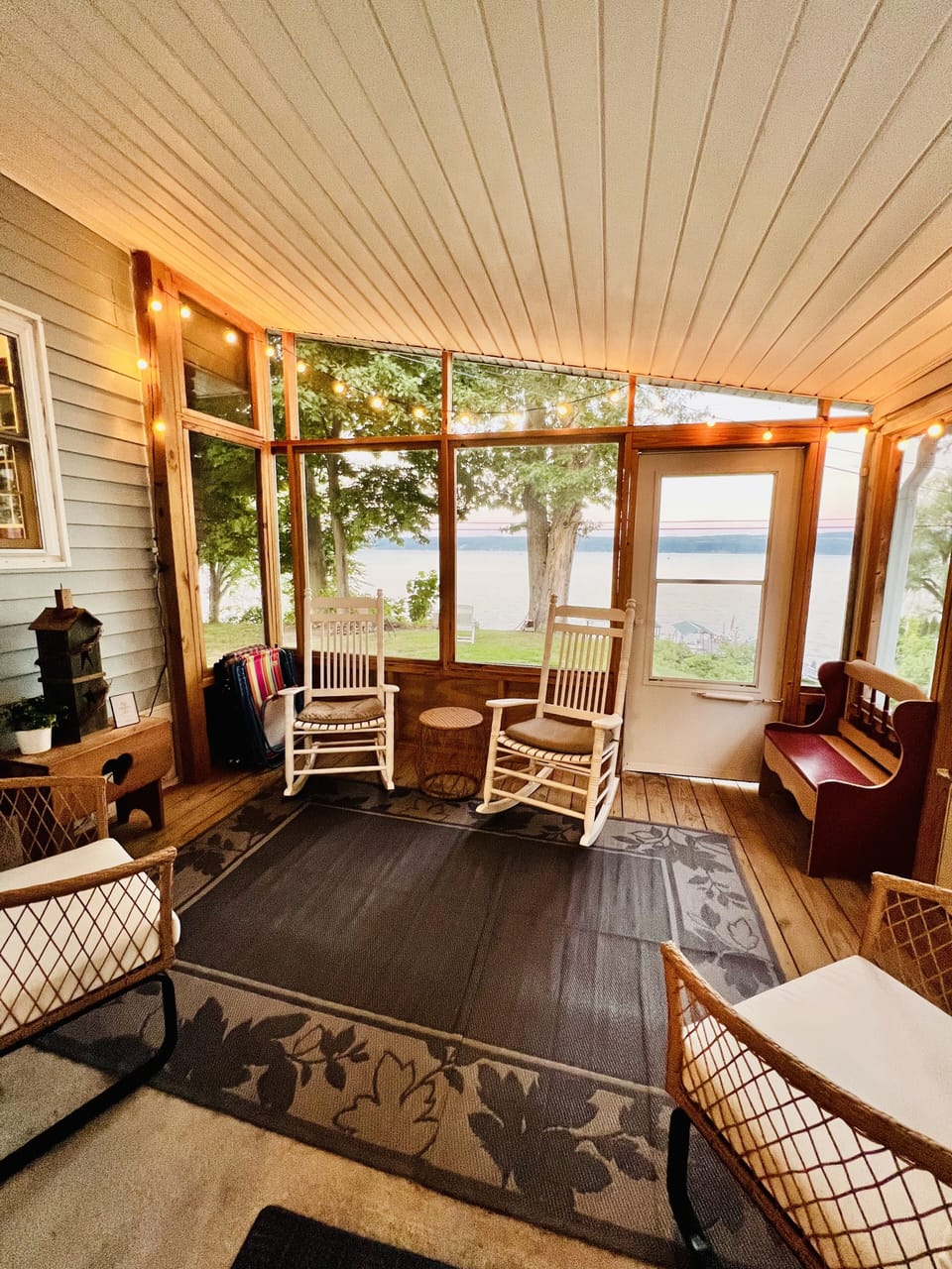 Screened in porch with bistro lights & rocking chairs overlooking the lake