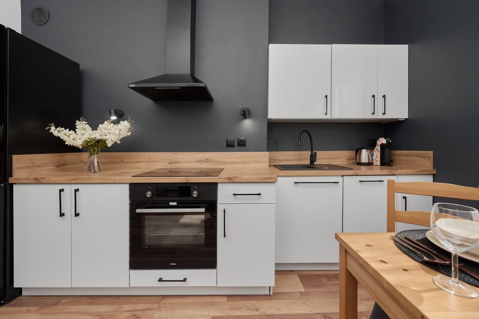 A modern kitchen with white cabinets, black accents, and a wooden dining table.