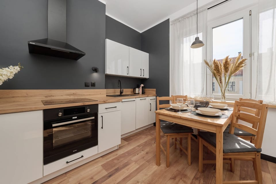 A modern kitchen with white cabinets, black accents, and a wooden dining table.