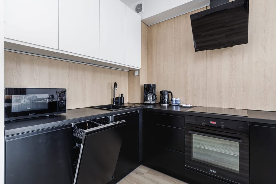 A compact kitchen with modern appliances, including a coffee maker and an electric kettle, on a light wood countertop.